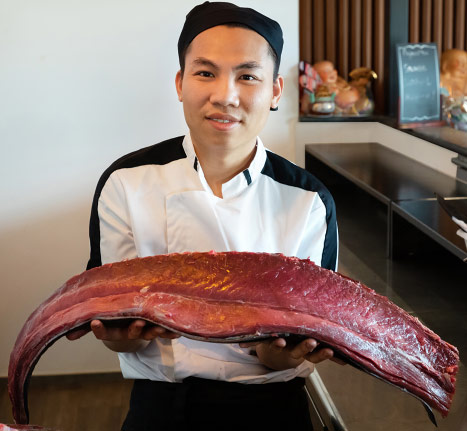 Un cuisinier asiatique tient dans les mains un gros filet de thon rouge