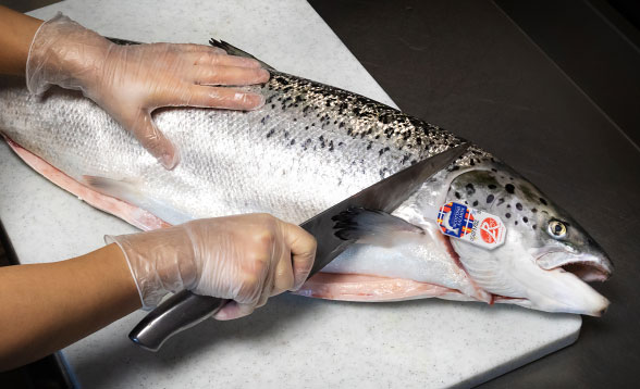 une main tient un couteau au dessus d'un saumon sur une planche à découper